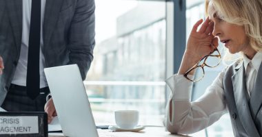 Panoramic shot of businesswoman looking at laptop near folder with crisis management and businessman